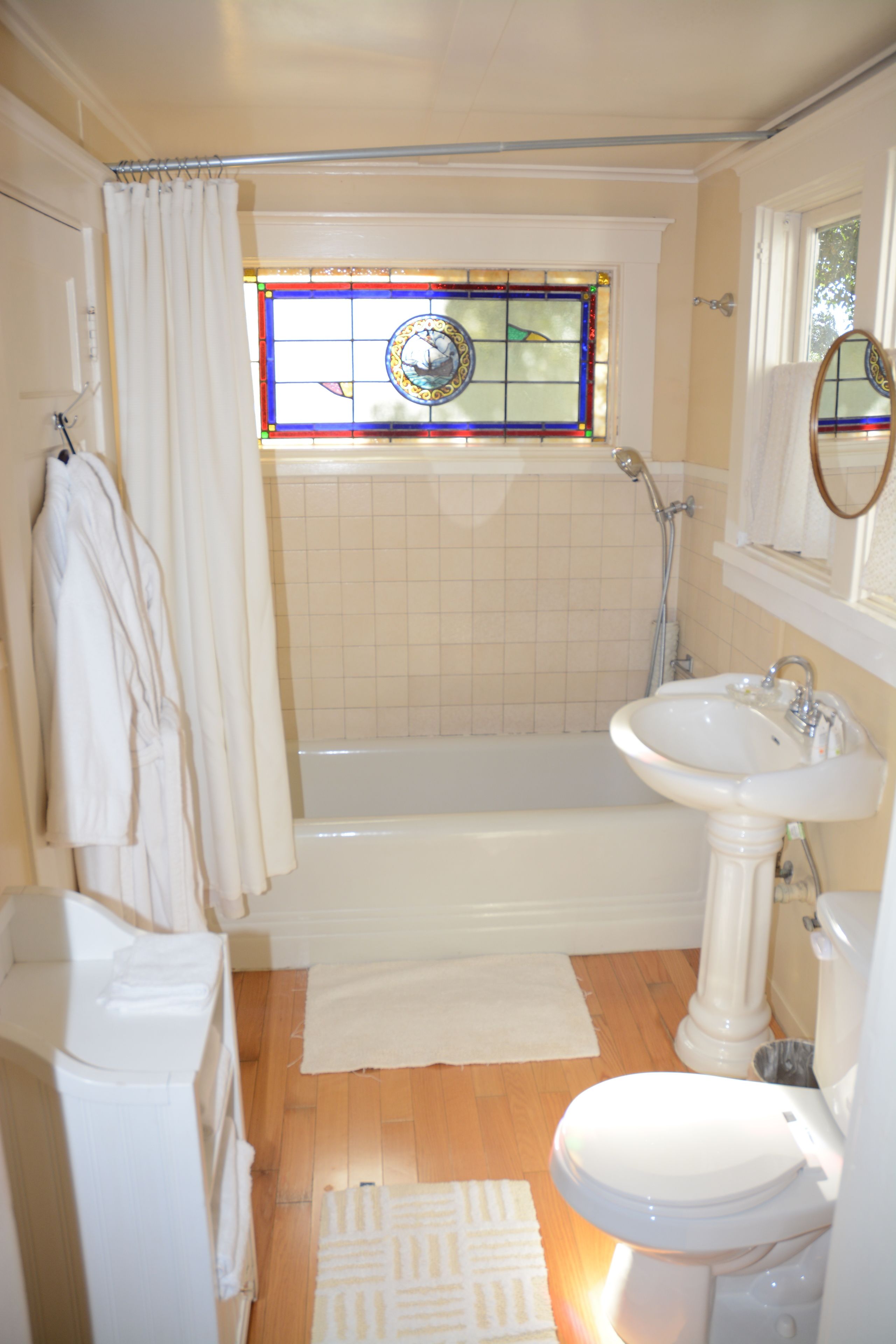 A bathroom with a bathtub, a sink, a toilet, a shower, and a stained glass window.