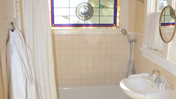 A bathroom with a bathtub, a sink, a toilet, a shower, and a stained glass window.