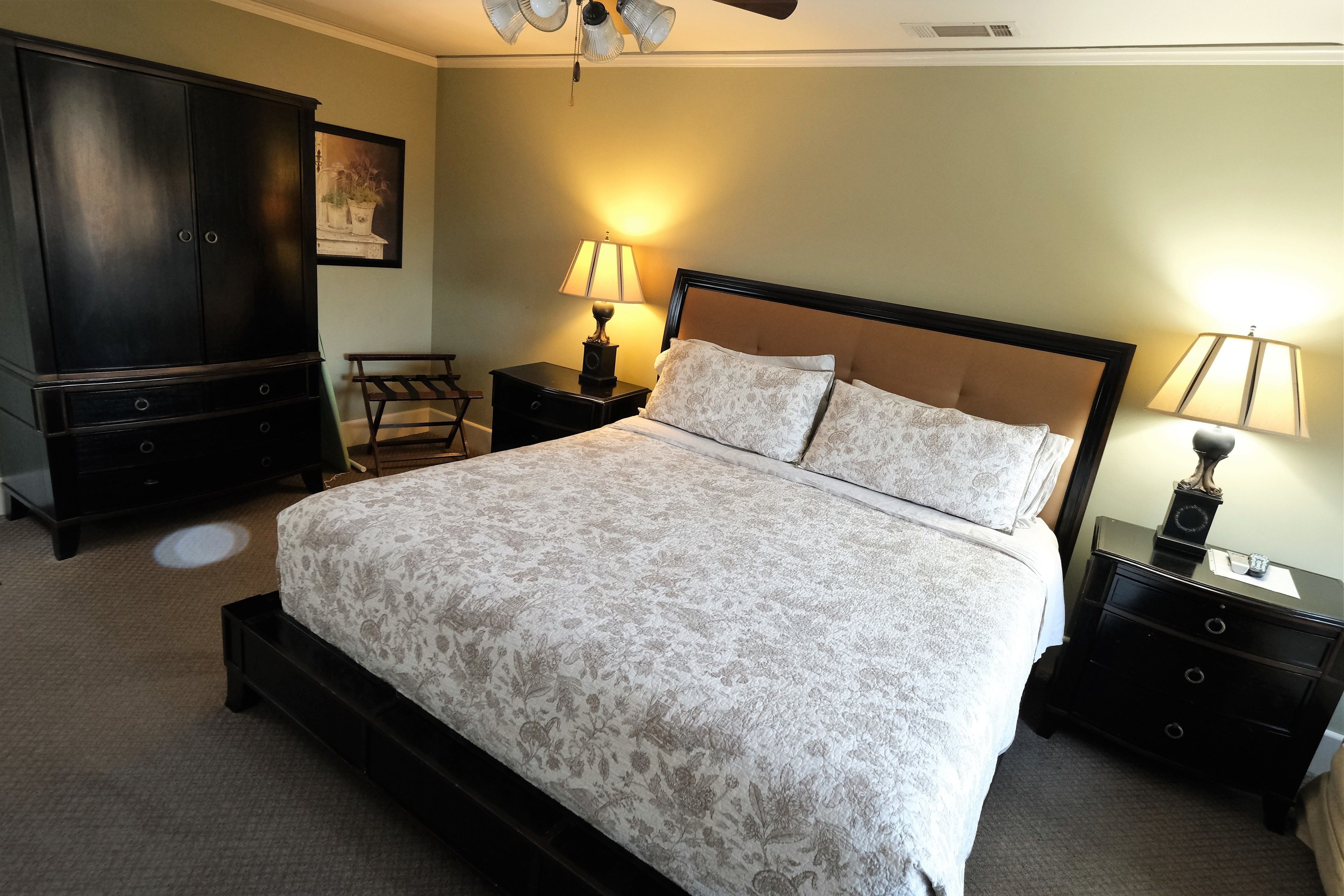 A bedroom with a large bed, two bedside tables, a nightstand, a wardrobe, and a ceiling fan.