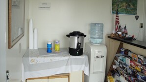 A kitchen with a coffee maker, a water dispenser, and a table with a white tablecloth. - Budget Motel (Grand Island)