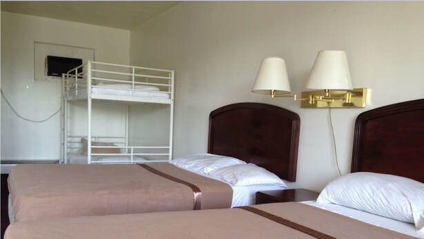 A hotel room with two beds, a bunk bed, and two wall-mounted lamps. - Budget Motel (Grand Island)