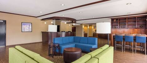 A lobby with a blue sectional sofa, green armchairs, a round coffee table, and a bar area with stools.