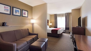 Une chambre d’hôtel avec un canapé, un lit, un bureau, une télévision et des tableaux encadrés au mur.