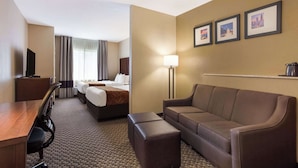 Une chambre d’hôtel avec un lit, un canapé, un bureau et une télévision. Trois tableaux encadrés sont accrochés au mur.