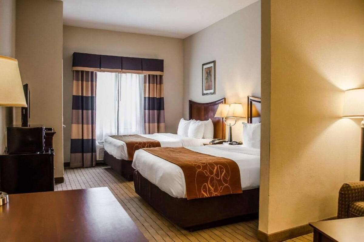 Una habitación de hotel con dos camas, un escritorio, una silla, una lámpara y una ventana con cortinas.