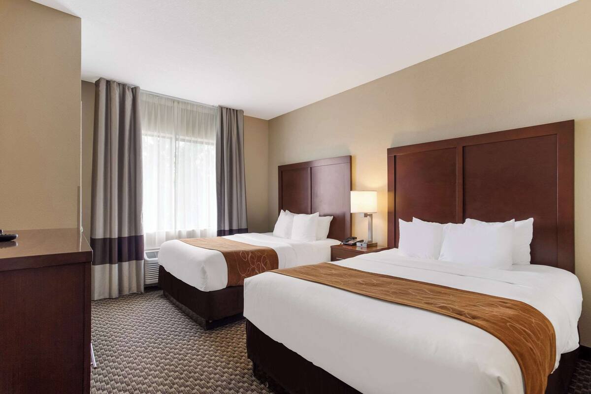 Habitación de hotel con dos camas, un escritorio, una lámpara y una ventana con cortinas.