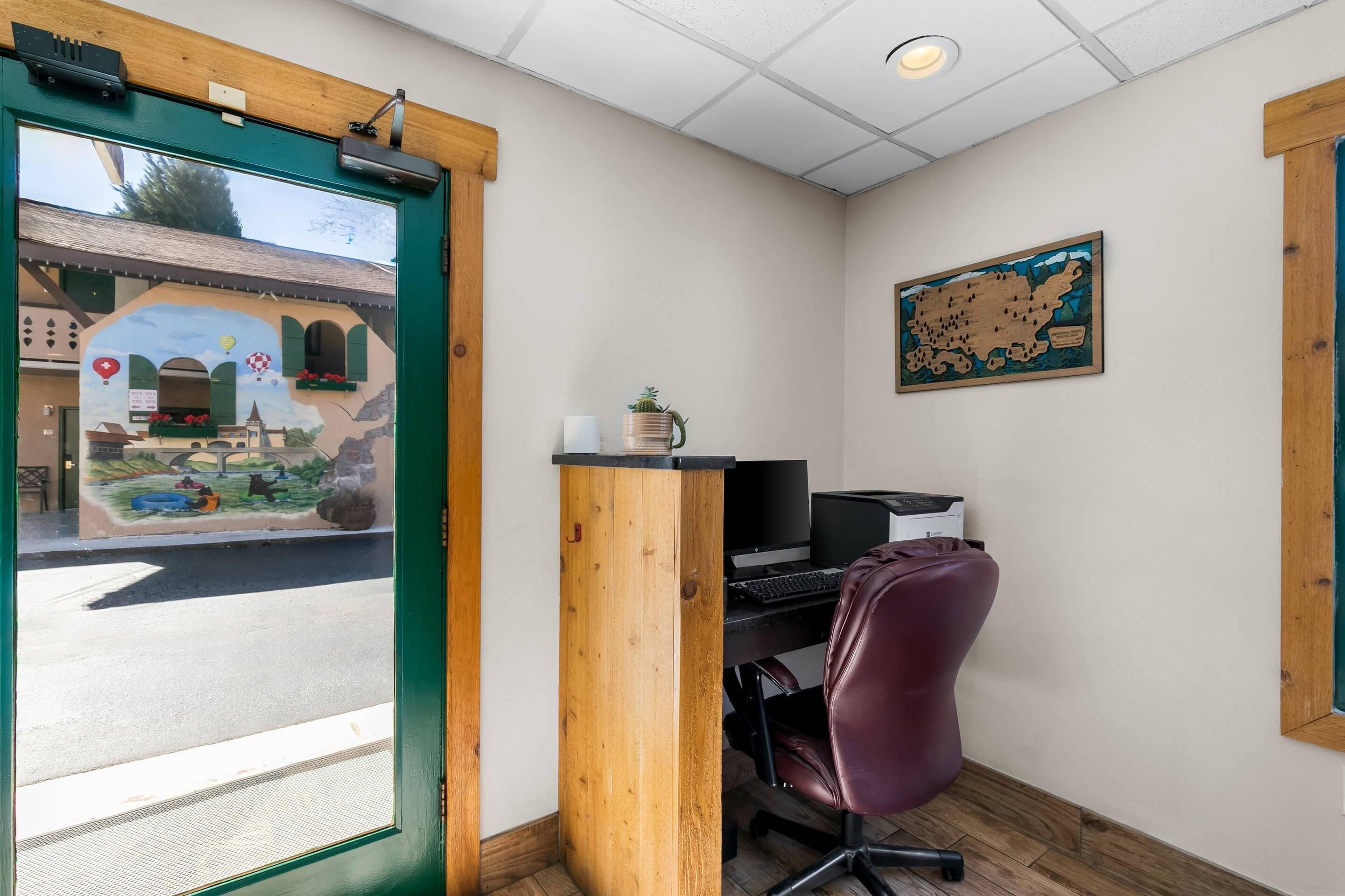 Una habitación con un escritorio, computadora y una silla. Se ve un edificio a través de la ventana.