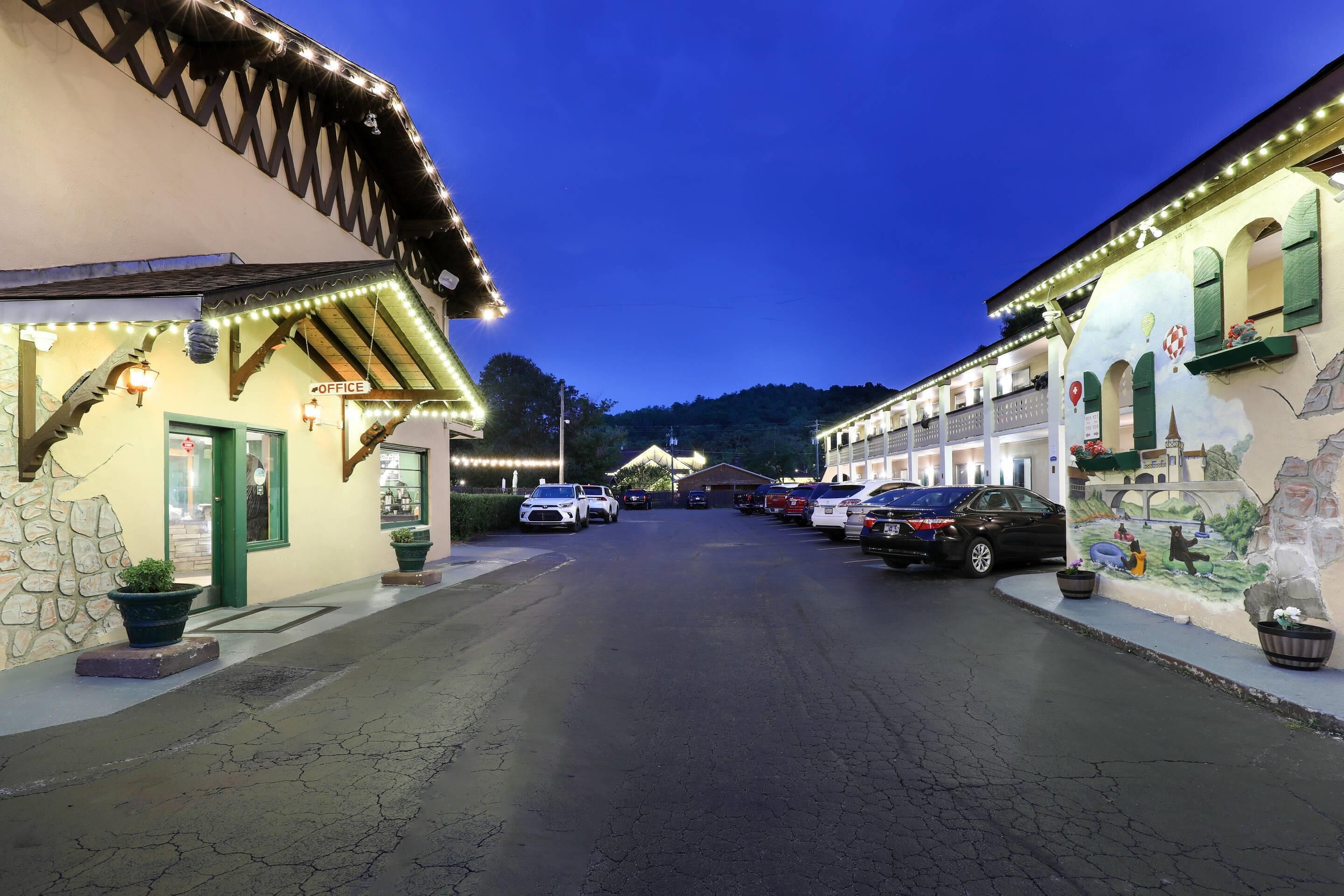 Calle con automóviles estacionados y edificios con letreros iluminados, incluyendo un letrero que dice 'OFFICE'.