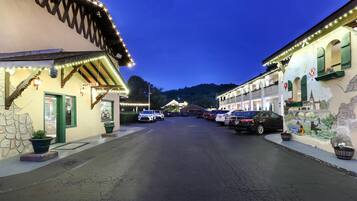 Calle con automóviles estacionados y edificios con letreros iluminados, incluyendo un letrero que dice 'OFFICE'.