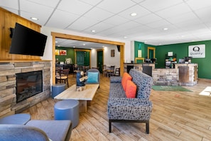 A modern hotel lobby with a stone fireplace, a flat-screen TV, a reception desk, and a seating area with a patterned sofa and ottoman. - Quality Inn Downtown Helen (Helen)