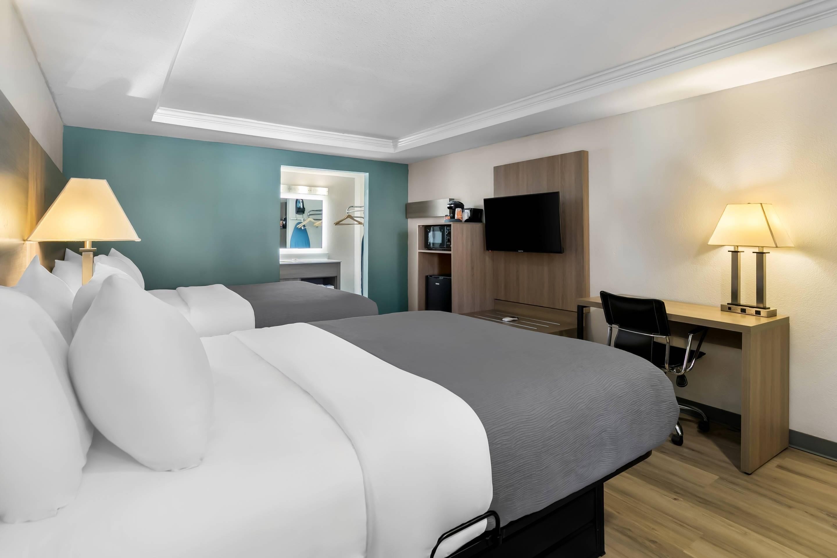 A hotel room with a bed, a desk, a chair, a TV, and a mirror.