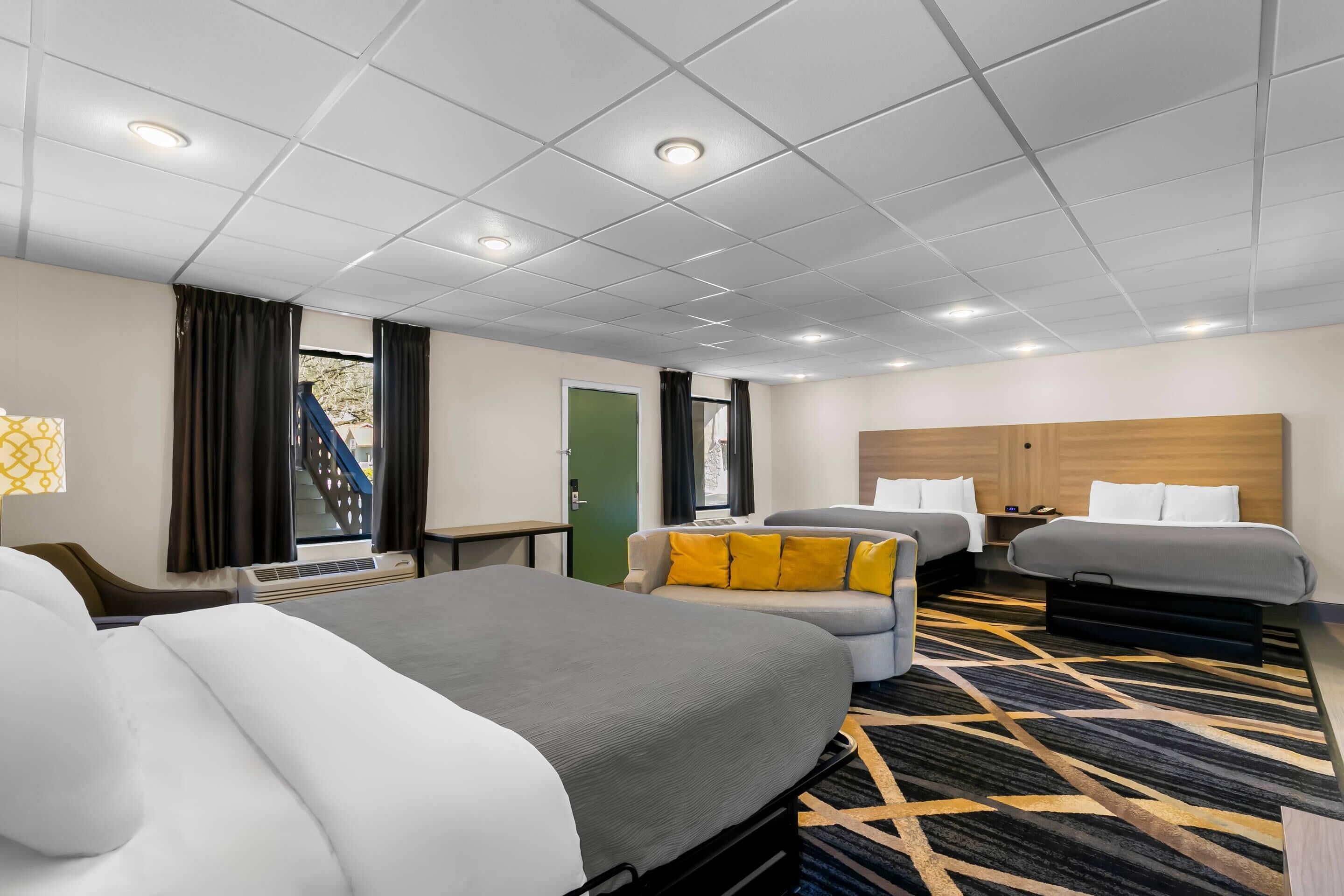 Een hotelkamer met twee bedden, een bank, een bureau en een raam met gordijnen.