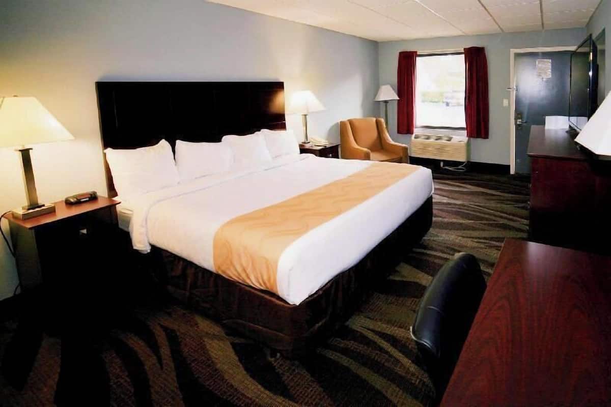 A hotel room with a large bed, two bedside tables with lamps, a chair, a desk, and a television.
