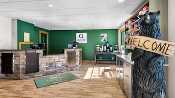 A reception area with a stone wall, a wooden bear sculpture, a welcome sign, and a coffee station.