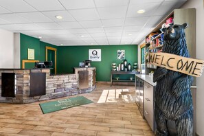 A reception area with a stone wall, a wooden bear sculpture, a welcome sign, and a coffee station.