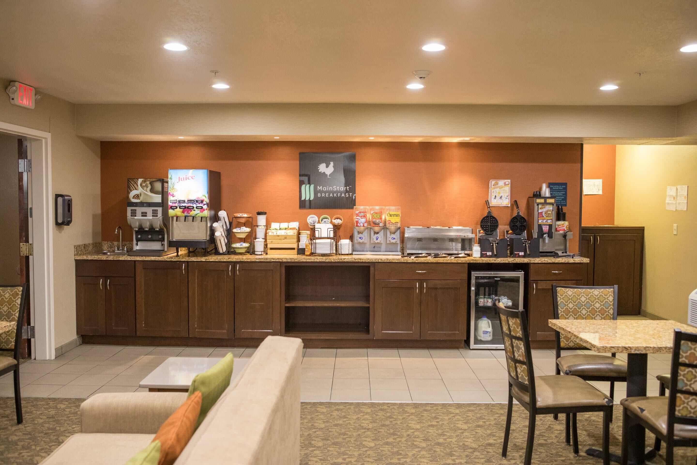 A hotel breakfast area with a counter, coffee machines, and seating.