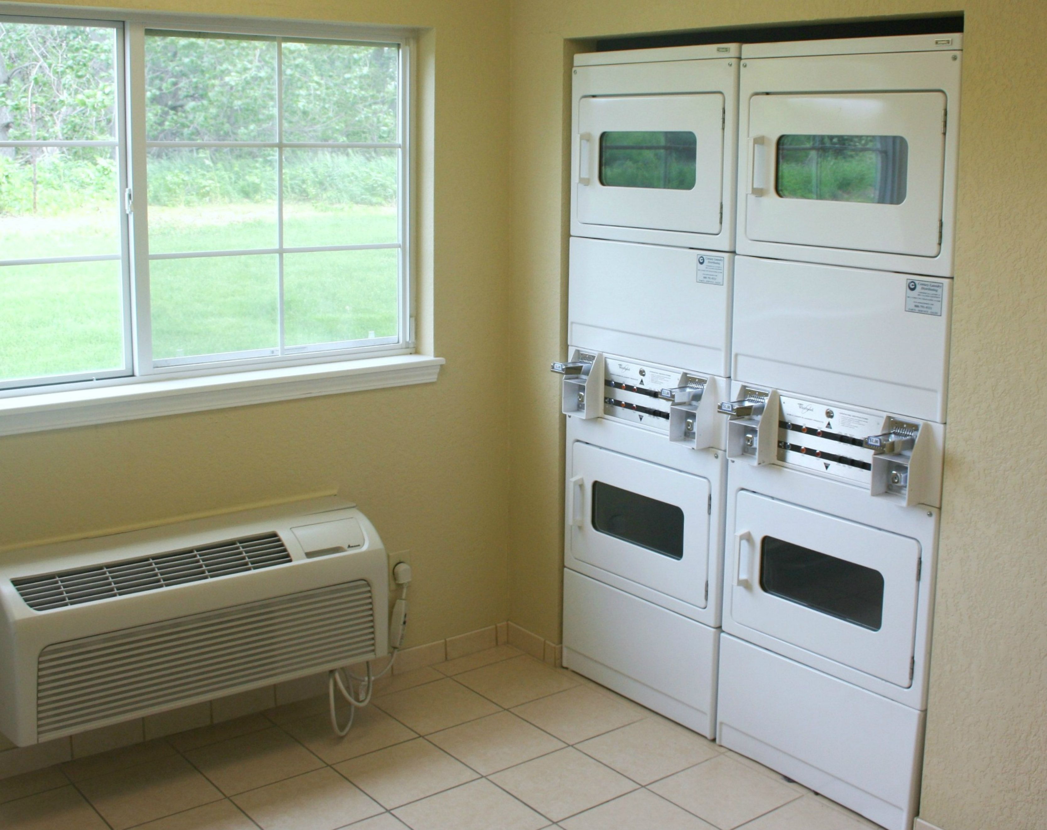 A laundry room with stacked dryers, a window, and a wall-mounted air conditioner.