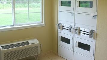 A laundry room with stacked dryers, a window, and a wall-mounted air conditioner.