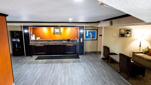Un moderno vestíbulo de hotel con mostrador de recepción central, zona de estar y kitchenette.