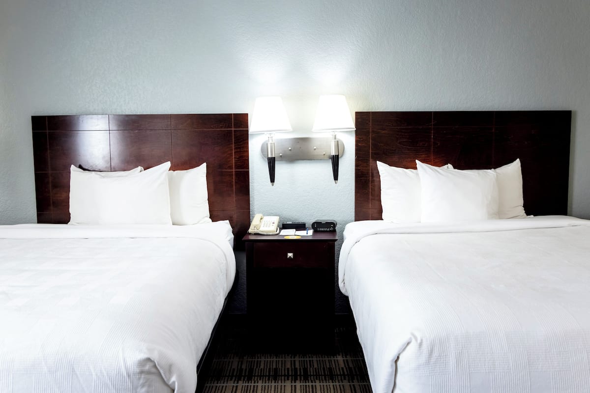 Une chambre d’hôtel avec deux lits, une table de chevet avec un téléphone et une lampe, et un luminaire fixé au mur.