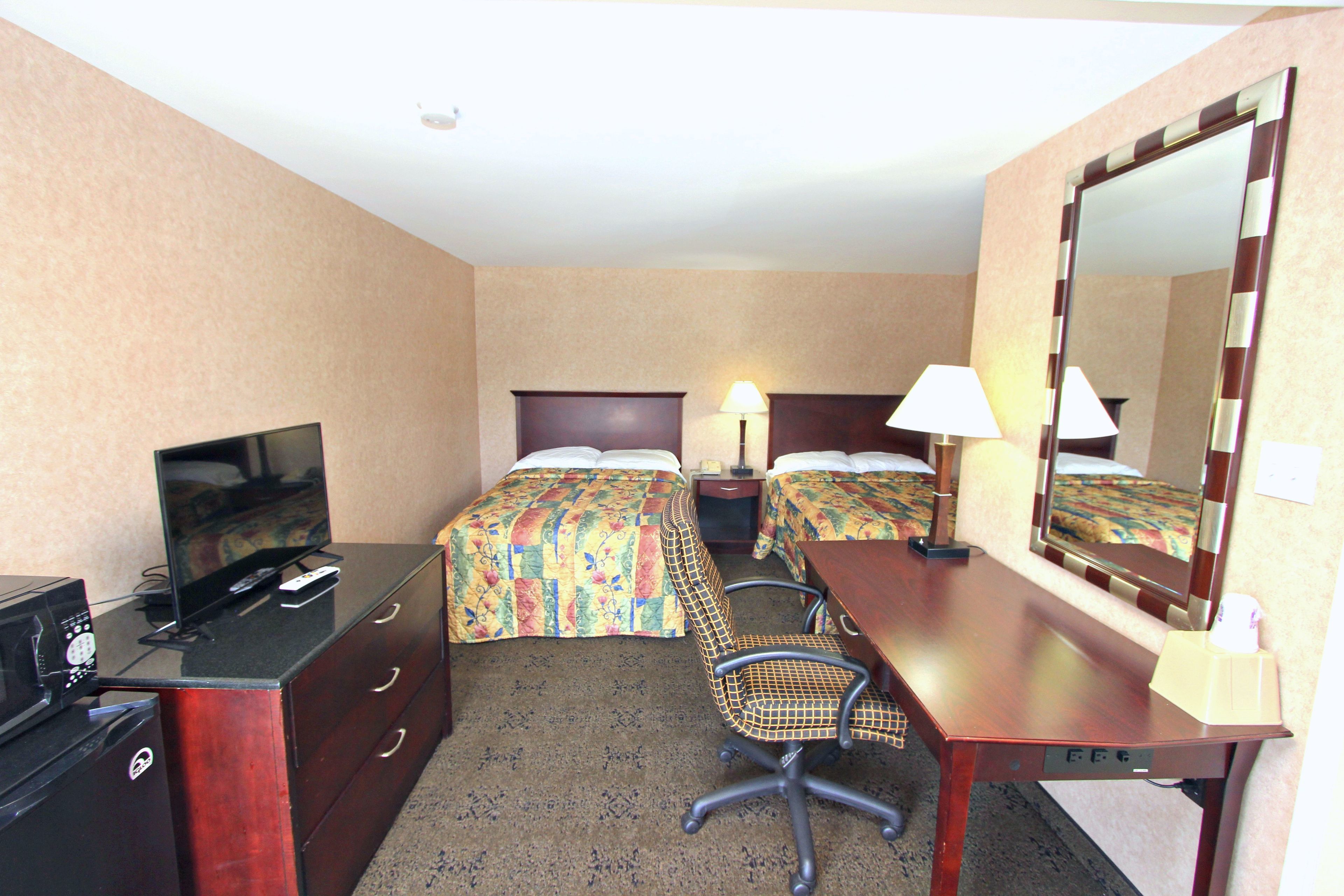 A hotel room with two beds, a desk, a chair, a television, and a mirror.