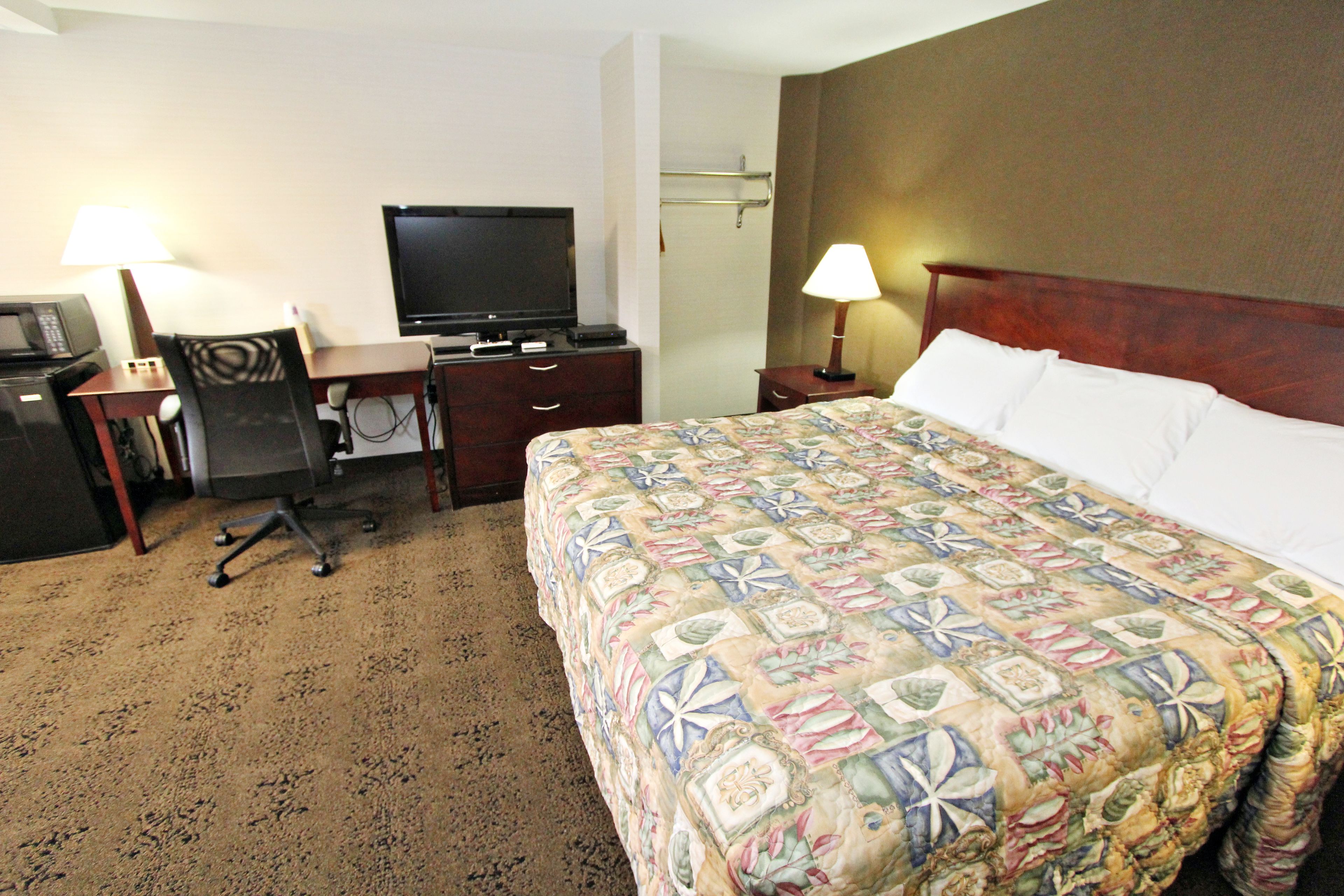 Una habitación de hotel con cama, escritorio, silla, televisor y dos lámparas.