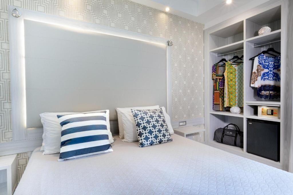 Ein Hotelzimmer mit Bett, Kissen, einem Kleiderschrank mit Kleidung und einem kleinen Tisch.