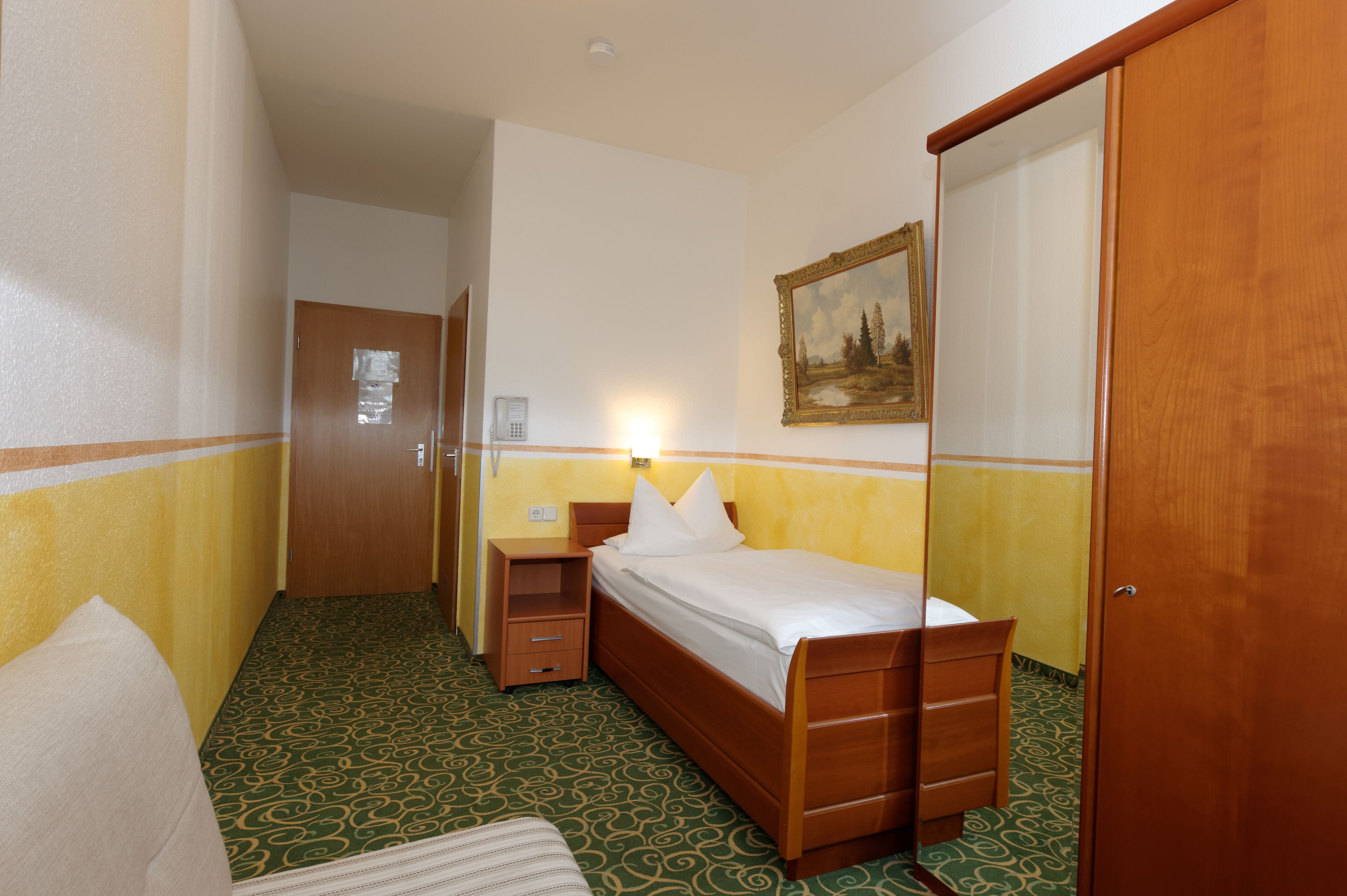 Habitación de hotel con una cama individual, una mesita de noche, un espejo y una puerta.