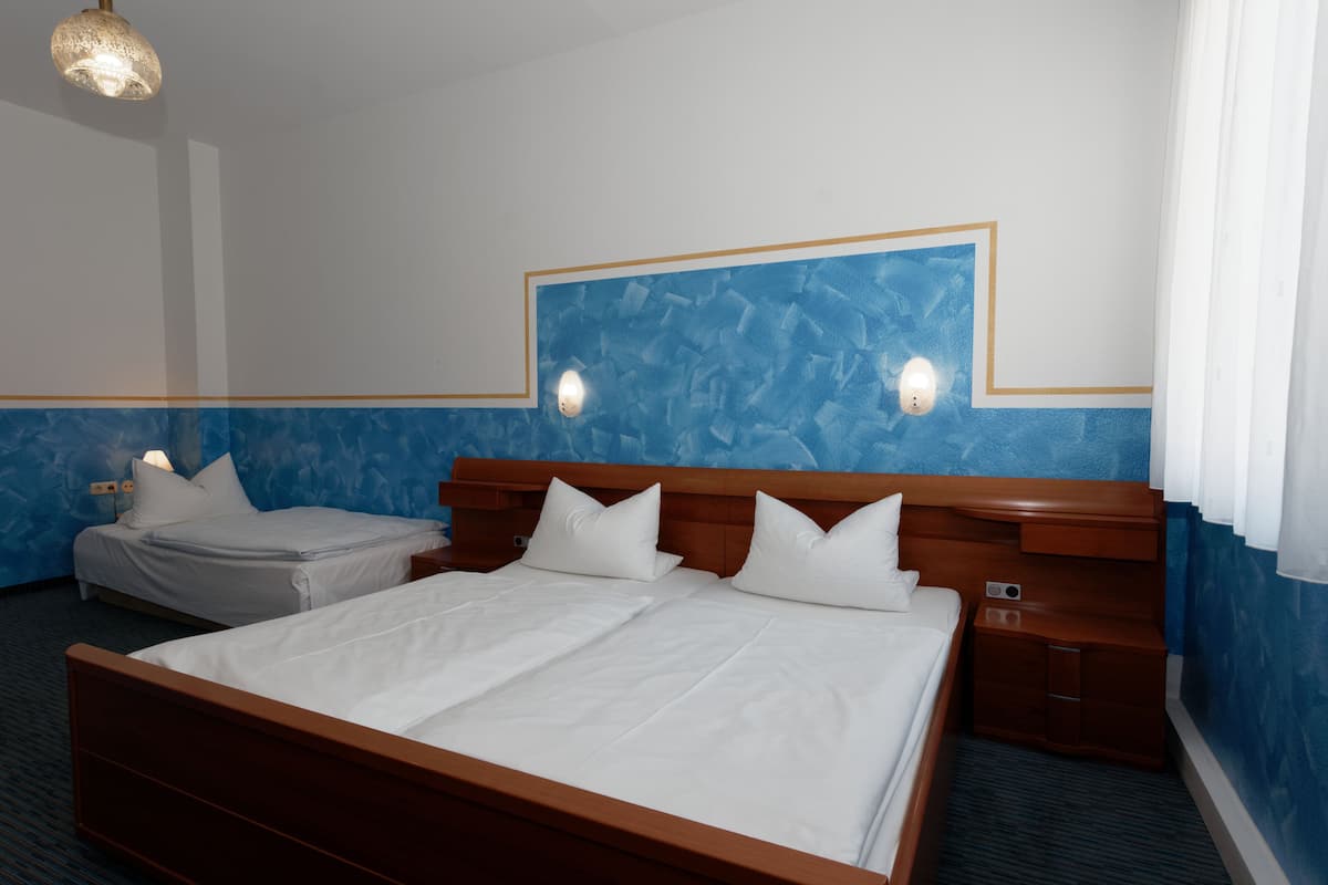 A hotel room with a large bed, two bedside tables, a nightstand, and a wall-mounted light fixture.