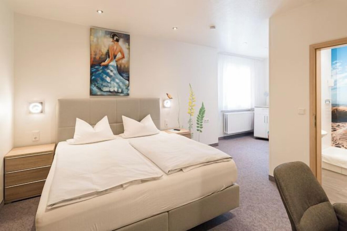 Une chambre d’hôtel moderne avec un grand lit, des tables de chevet, un tableau au mur et une vue par la fenêtre.