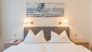 A neatly made bed with white linens and pillows, a headboard with a textured pattern, two bedside lamps, and a painting of sailboats on the wall. - PrivatHotel Probst (Nuremberg)