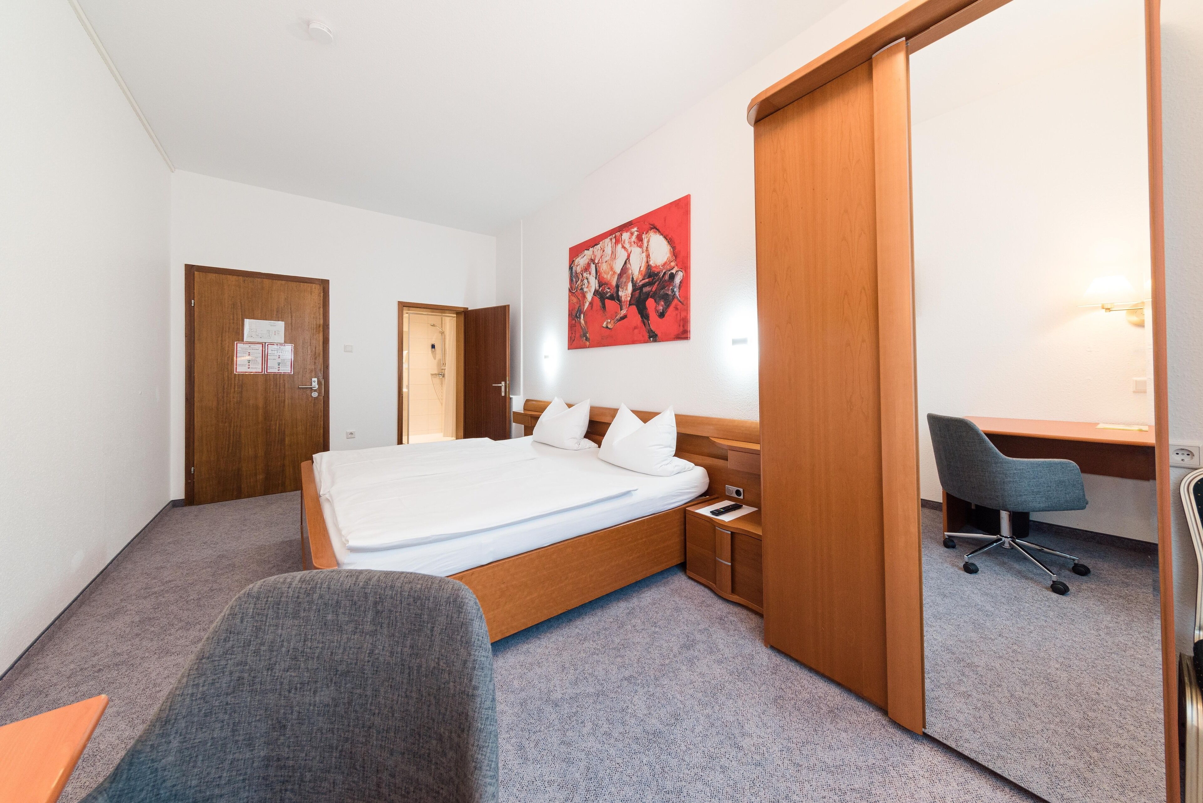 A hotel room with a bed, a desk, a chair, and a painting on the wall.