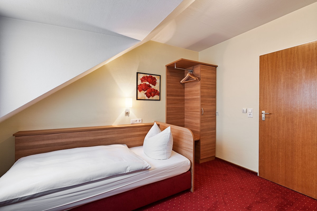Een slaapkamer met een bed, een houten kledingkast, een rode vloerbedekking en een wandlamp.