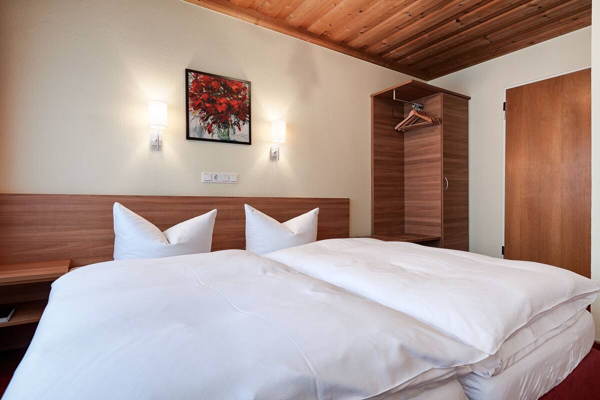 Een hotelkamer met een groot bed, een houten hoofdbord, twee wandlampen, een schilderij, een kledingkast en een kapstok.