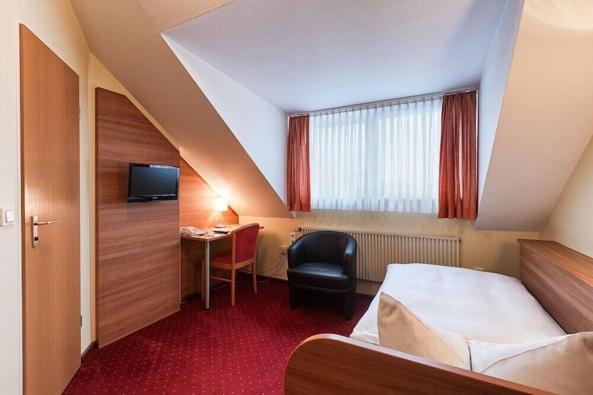Een hotelkamer met een bed, een bureau met stoel, een televisie en een raam met gordijnen.