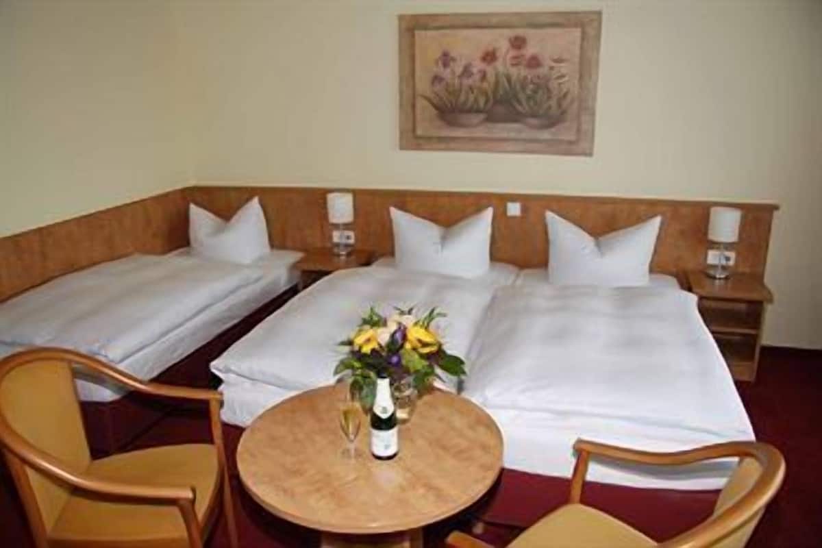 Een hotelkamer met twee eenpersoonsbedden, een klein rond tafeltje met een bloevas en twee stoelen.