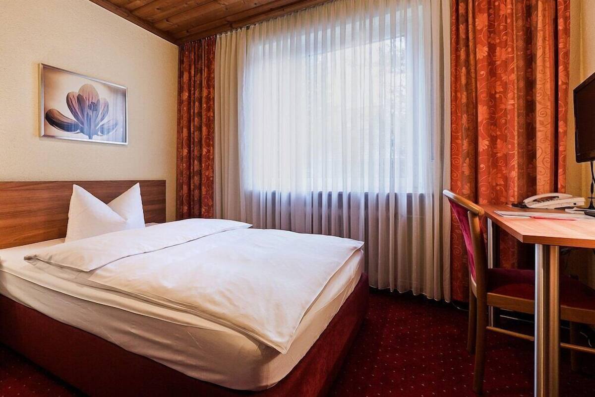 Hotelkamer met een bed, bureau, stoel, televisie en raam met gordijnen.