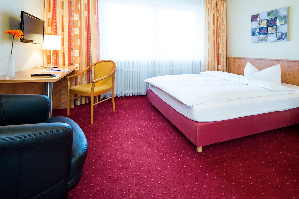Een hotelkamer met een bed, een bureau met stoel, een televisie en een raam met gordijnen.