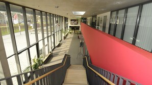 A corridor with large windows, a red wall, and a staircase.