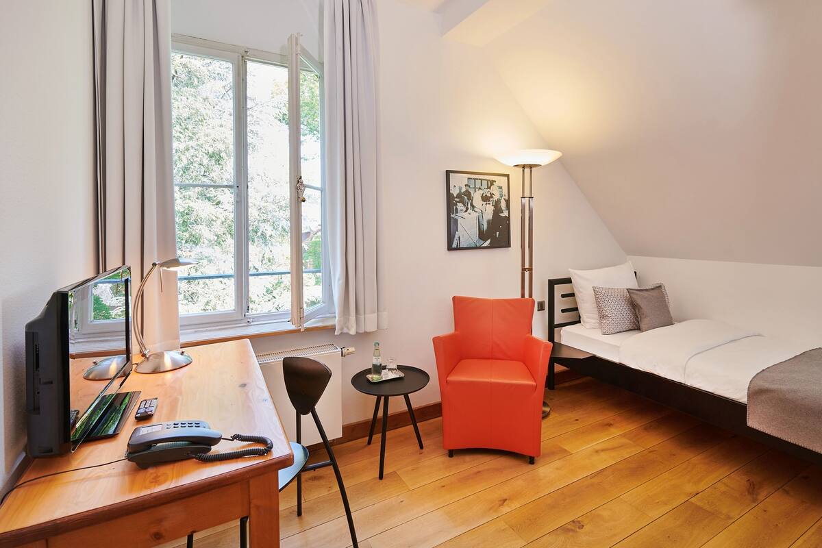 A bedroom with a bed, a desk with a computer, a chair, and a lamp.