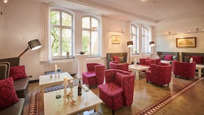 A hotel room with a seating area featuring red upholstered chairs, a white table with a wine glass, candles, and a bottle of wine. - Hotel MutterHaus Düsseldorf (Düsseldorf)