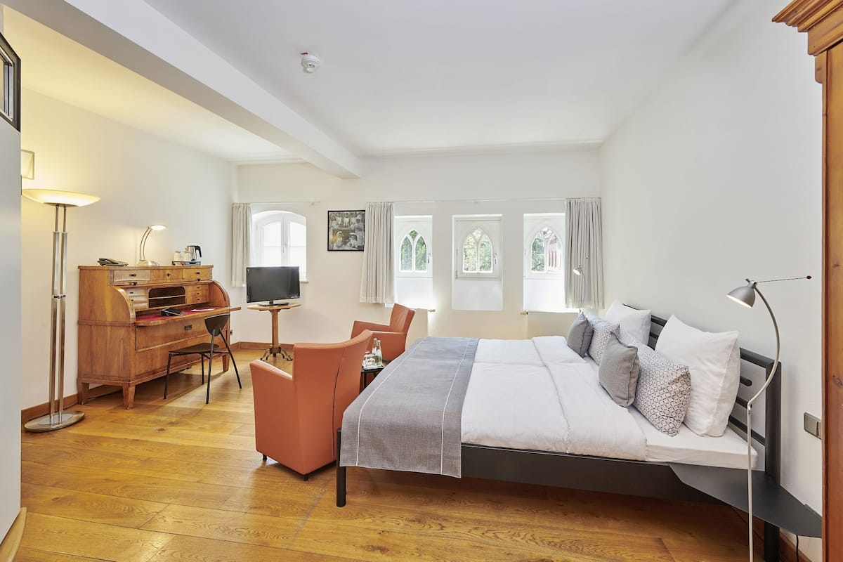 A spacious bedroom with a large bed, a desk, a chair, and a television.