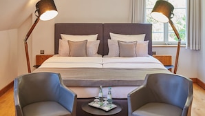 A double bed with a headboard, two bedside lamps, two armchairs, a small round table with a tray of glasses and bottles, and a window with curtains. - Hotel MutterHaus Düsseldorf (Düsseldorf)