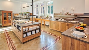 A modern kitchen with a buffet setup, wooden cabinets, and large windows. - Hotel MutterHaus Düsseldorf (Düsseldorf)