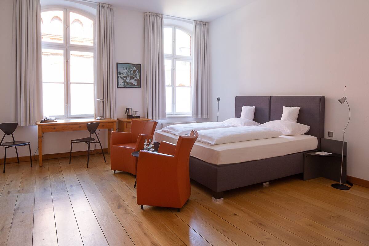 A hotel room with a large bed, two chairs, a desk, and a window with curtains.