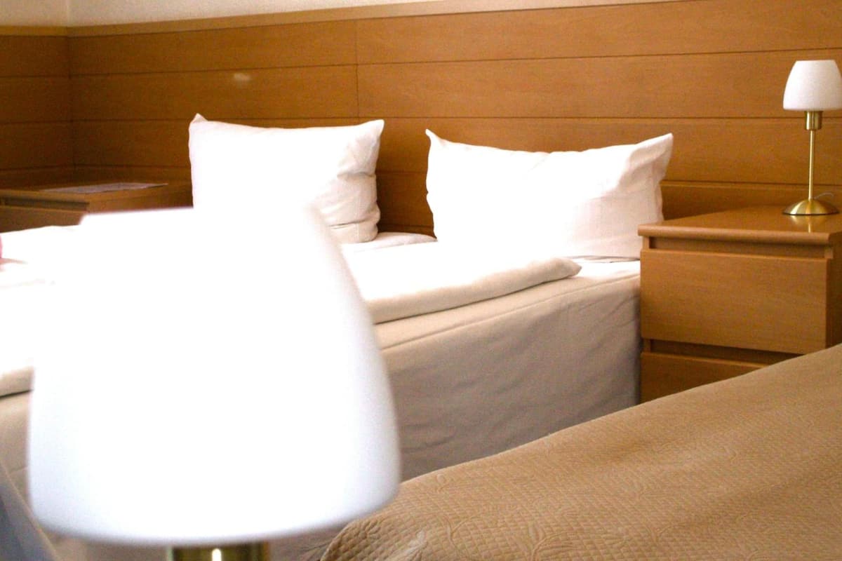 A hotel room with a bed, a bedside table with a lamp, and a nightstand.
