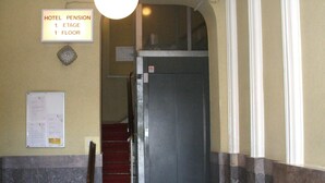 A hotel lobby with a red carpeted staircase, a sign indicating the location of the hotel pension on the first floor, and a wall-mounted light fixture. - Pension Messe am Funkturm (Berlin)