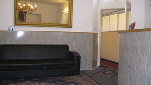 A black sofa, a large mirror, and a patterned rug in a room with marble walls and a wooden floor. - Pension Messe am Funkturm (Berlin)