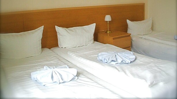 A hotel room with two beds, a wooden headboard, white linens, and a bedside lamp. - Pension Messe am Funkturm (Berlin)