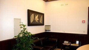 A room with a dark brown leather sofa, a potted plant, a framed botanical print on the wall, a small table with books, and a white door. - Hotel Rheinischer Hof (Düsseldorf)